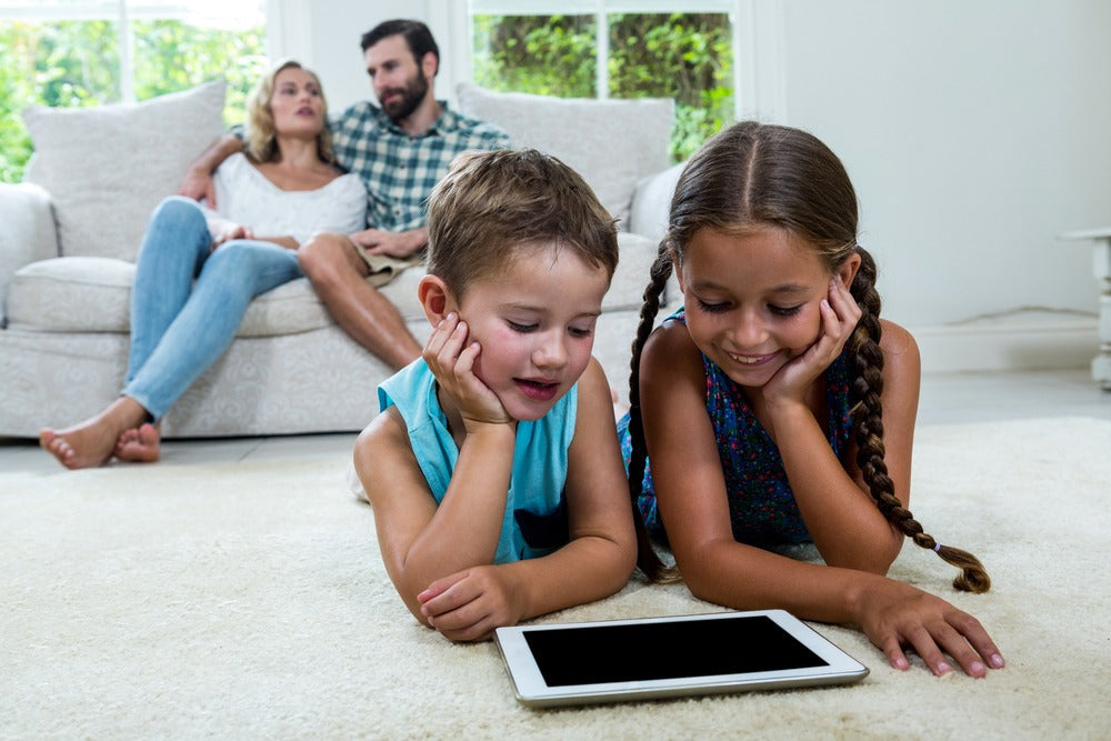 2 children having screen time with parents in background